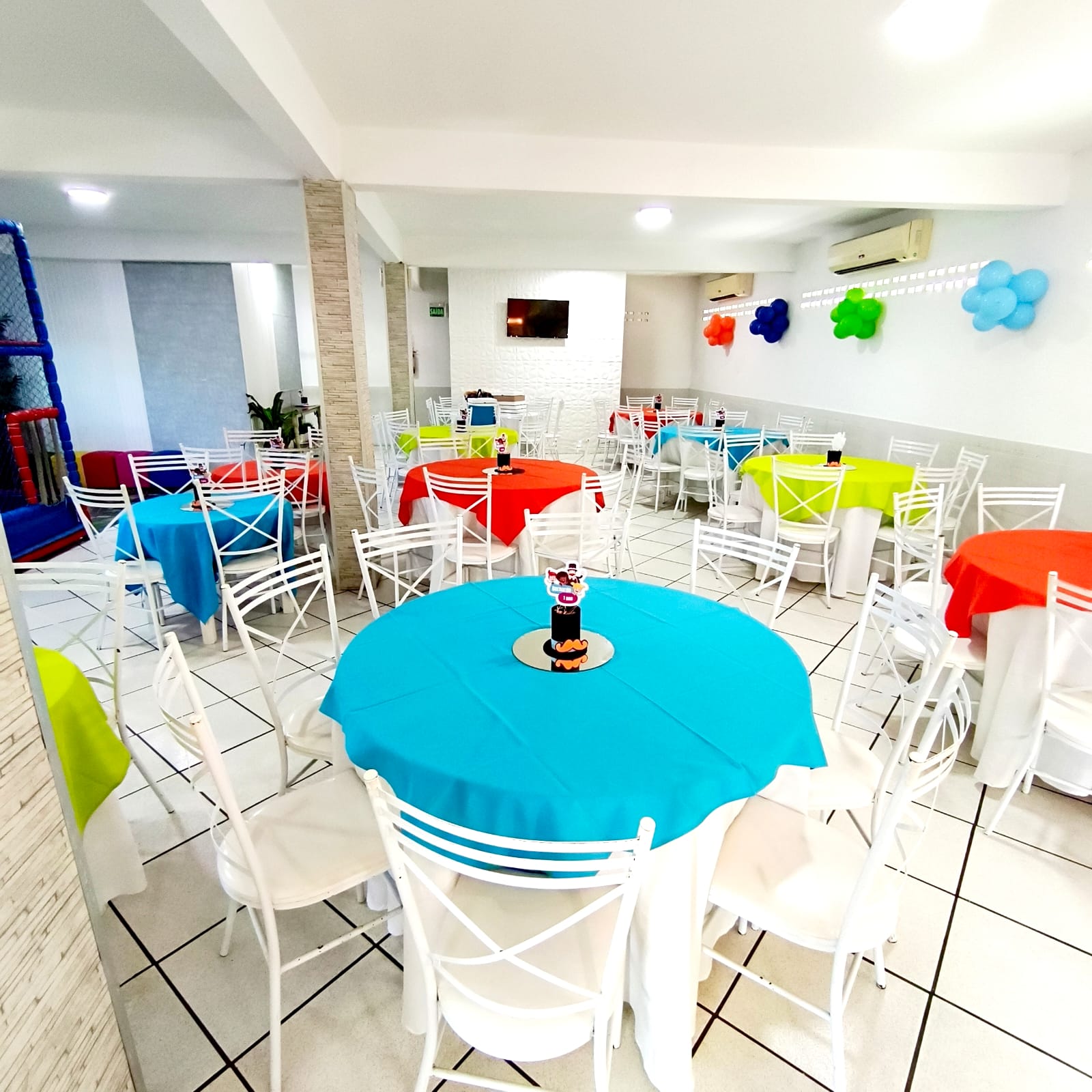 Mesas e cadeiras coloridas montadas no salão da Miloca Festas